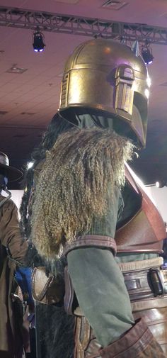 a man in a costume is standing next to a giant helmet on display at a museum