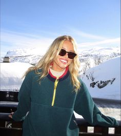 a woman wearing sunglasses standing in front of snow covered mountains