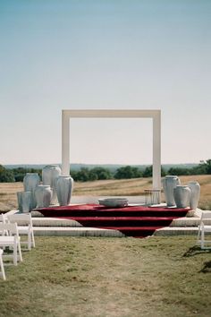 an outdoor ceremony setup with white chairs and vases on the table in front of it