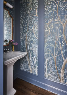 a bathroom with blue walls and wallpaper that has trees on it, as well as a sink