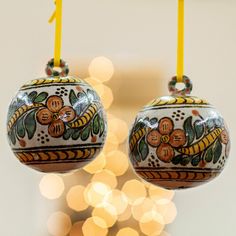 two ornaments hanging from strings with lights in the background