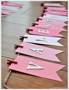 pink and white paper pennants with letters on them sitting on a wooden floor next to string