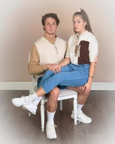 a man and woman sitting on a white chair in front of a wall with a wooden floor