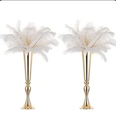 two tall gold vases with white feathers in them on a white background for decoration