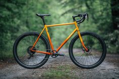 an orange bike parked on the side of a dirt road in front of some trees