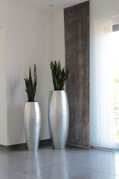 two large silver vases with plants in them on the floor next to a window