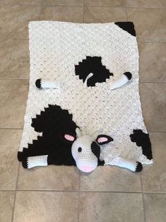 a black and white cow is laying on the floor next to a crocheted blanket