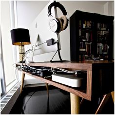 a computer desk with headphones on it and a lamp next to it in front of a bookshelf