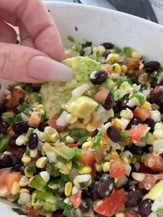 a person dipping a tortilla chip into a bowl filled with corn, black beans and avocado