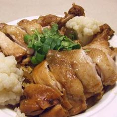 a white plate topped with chicken, cauliflower and green garnishes