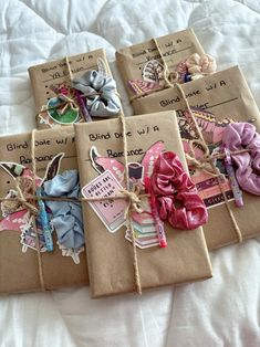 four wrapped gift bags with ribbons and tags on them sitting on a white bed sheet