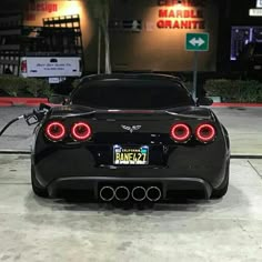 the back end of a black sports car parked in front of a parking lot at night