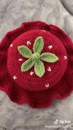 a crocheted red flower with green leaves on it's center sits on a gray surface