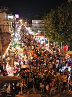 a large group of people standing in the middle of a street at night with lights on