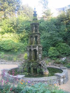 an old water fountain surrounded by flowers and trees