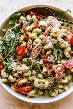 a white bowl filled with pasta salad topped with tomatoes and spinach