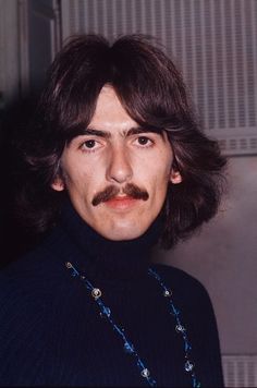 a man with long hair and a moustache wearing a blue turtle neck sweater