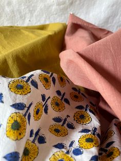 two different colored fabrics are laying next to each other on a white tablecloth with yellow and blue flowers