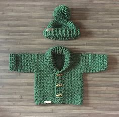 a green knitted sweater and hat sitting on top of a wooden floor next to a wall