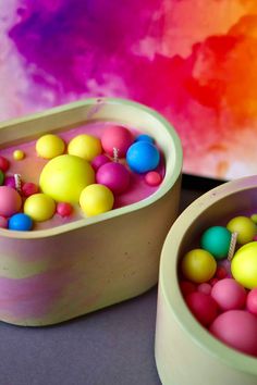 two bowls filled with candy balls on top of a table next to a rainbow colored wall