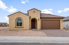 a tan house with a red door and brown shutters on the front, in an empty lot