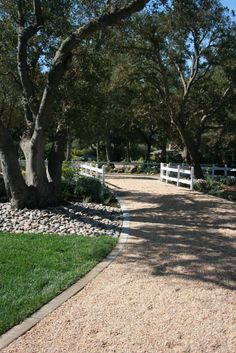 there is a white fence in the middle of this path that leads to some trees