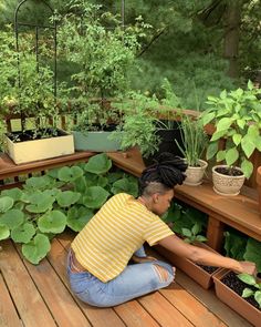 a woman kneeling down in front of some plants on a wooden deck with potted plants