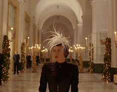 a woman in a black dress and white hair is walking through a hallway with christmas lights