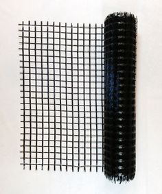 a piece of black wire mesh sitting on top of a white table next to a roll of yarn