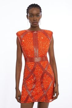 a model wears an orange dress with sequins on it and stands in front of a white background