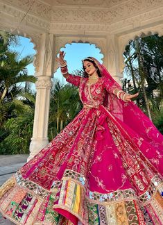 a woman in a pink lehenga dancing on the ground with palm trees behind her