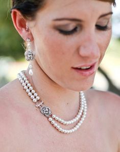 a woman wearing a necklace and earrings with pearls on her neck, looking down at the ground