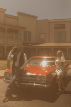 two people sitting on the hood of a red car