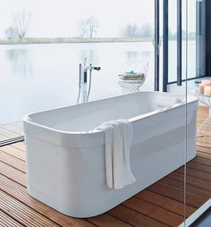 a large white bathtub sitting on top of a wooden floor next to a window