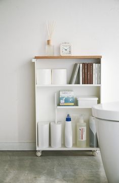 a white shelf with various bathroom items on it next to a bathtub and toilet