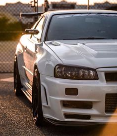 a white car parked on the side of a road next to a chain link fence