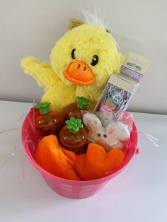 a yellow stuffed duck sitting in a pink basket filled with toys and candy items,