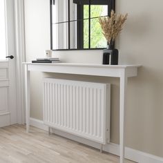 a white console table with a mirror and vase on it in front of a window