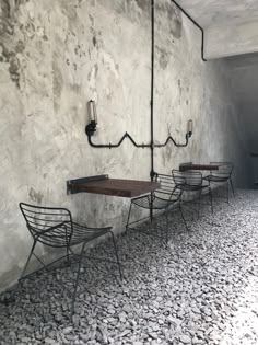 three metal chairs sitting next to each other in front of a wall with exposed pipes