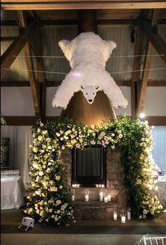 a large teddy bear hanging from the ceiling above a fireplace with flowers and candles around it