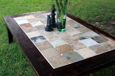 a wooden table with chess pieces and vases on it, sitting in the grass