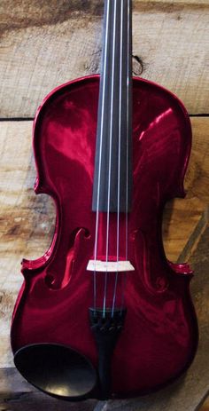 a red violin sitting on top of a wooden table