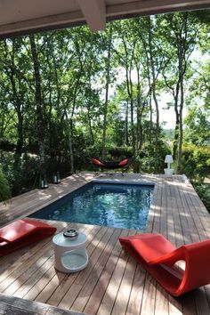 a deck with two chairs and a pool in the back ground, surrounded by trees