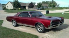 a red car parked on the side of a road in front of a house and grass