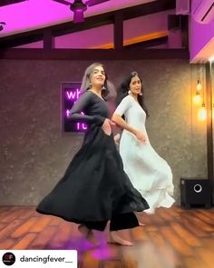 two women in long dresses are dancing on a wooden floor with purple lights behind them