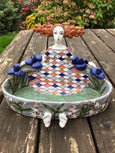 a ceramic sculpture sitting on top of a wooden table next to flowers and trees in the background