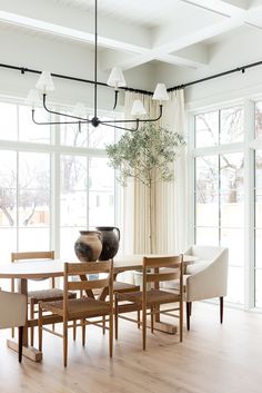 a dining room table with chairs and a vase on top of it in front of large windows