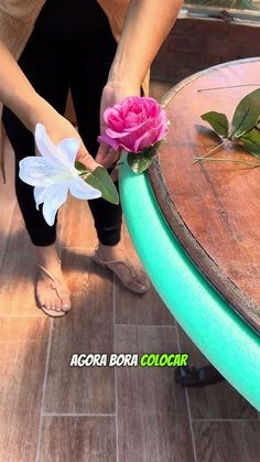 a woman holding a flower on top of a wooden table next to a green chair