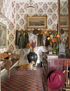 a room with wallpaper and pictures on the walls, including a dog laying in front of a vase