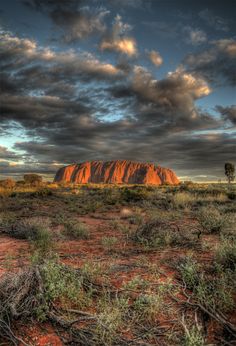 the red rock is surrounded by scrub brush and green plants under a cloudy sky with clouds